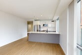 Located in Cambridge's vibrant Kendall Square, this modern two-bedroom, two-bathroom residence offers a thoughtfully designed single-level layout with clean lines and a contemporary aesthetic throughout. Light wood flooring flows seamlessly across the entire unit, complementing the bright white walls and creating a warm, cohesive atmosphere.

The open-concept living, dining, and kitchen area forms the heart of the home. The kitchen features sleek white cabinetry, a white quartz peninsula with an undermount sink and matte black faucet, stainless steel appliances including a refrigerator, microwave, and range, and a subtle subway tile backsplash. Large windows in the kitchen and living area invite ample natural light and frame views of the surrounding Cambridge cityscape.

Both bedrooms are generously proportioned, each benefiting from oversized windows with urban views. The primary bedroom includes a spacious double-door closet and sliding floor-to-ceiling windows that overlook the skyline. The second bedroom is equally bright with large windows. Three closets throughout the unit provide substantial storage.

The two bathrooms are finished in a modern style, featuring taupe floating vanities with white countertops, matte black fixtures, frameless mirrors, and wood-toned flooring. One bathroom includes a glass-enclosed walk-in shower. The unit also includes a dedicated laundry area, completing this well-appointed urban residence.