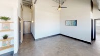 This single-floor space showcases a distinctive loft-inspired design that blends industrial and contemporary elements throughout. The main living area commands immediate attention with its dramatically high ceilings, polished concrete floors, and an exposed structural ceiling featuring visible ductwork and support beams — hallmarks of converted industrial architecture. A ceiling fan is centrally mounted, and abundant natural light filters through a bank of large windows framed in warm wood, offering views of the surrounding streetscape.

The kitchen is well-appointed, featuring dark espresso cabinetry that reaches toward the elevated ceiling, granite countertops, a subway tile backsplash, and a full suite of stainless steel appliances including a refrigerator, electric range, microwave, and dishwasher. Pendant lighting and recessed fixtures illuminate the workspace effectively.

Two bathrooms mirror each other in design, each offering dark cabinetry with brushed nickel hardware, granite countertops with undermount sinks, wall-mounted mirrors, upper storage cabinets with display niches, and tile flooring. One bathroom includes a window, providing natural light.

Overall, the space presents an open, airy industrial-chic aesthetic with refined finishes throughout.