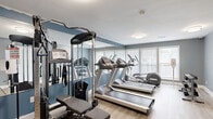 Located at 3200 Lakeview Pl in East Point, Georgia, this fitness center is a well-equipped, single-room facility designed to support a well-rounded workout routine. The space features light wood-look flooring and two-tone blue-gray walls that create a clean, modern aesthetic throughout.

The room is outfitted with a multi-station cable machine with an adjustable bench, providing options for a wide range of strength training exercises. Cardio equipment includes multiple treadmills and an elliptical trainer, positioned along the windowed wall to take advantage of natural light. A dumbbell rack with a full set of free weights rounds out the strength training offerings. A hand sanitizer station is also present, reflecting attention to cleanliness and user safety.

Large windows with white blinds line one wall, allowing ample natural light to fill the space, while flush-mounted ceiling lights ensure consistent illumination throughout the day and evening. Full-length mirrors along one wall visually expand the room and allow users to monitor their form during exercise. A water cooler is available for convenience. The single entry door and straightforward layout make for easy navigation, keeping the focus on fitness in an efficient and functional environment.