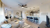 This thoughtfully designed single-floor residence offers a seamless open-concept layout that connects the living, dining, and kitchen areas into one cohesive, light-filled space. Light wood-tone flooring runs throughout, complementing the neutral white walls and creating a clean, modern aesthetic.

The living area is anchored by a ceiling fan with integrated lighting and features large windows dressed with sheer curtains that invite abundant natural light. The kitchen is a standout, boasting dark cabinetry, stainless steel appliances, a white subway tile backsplash, and a generous breakfast bar with seating for three, illuminated by elegant brass-accented pendant lights. An adjacent dining nook provides an intimate space for meals, complete with a rich wood dining table.

The bedroom is a serene retreat, offering a ceiling fan, large windows with floor-length drapes, and ample natural light. The primary bathroom features a walk-in glass shower, dark vanity cabinetry with a white countertop, and wood-look flooring. A second full bathroom includes a tub-shower combination, offering added convenience for guests. Throughout the residence, cohesive finishes and contemporary design choices create a polished, move-in-ready environment.