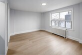 Located on the fifth floor of 262 Jarvis Street in downtown Toronto, this compact one-bedroom, one-bathroom unit offers a clean, minimalist interior designed to maximize its efficient footprint. The space is finished with light-toned hardwood flooring throughout, contributing to a bright and cohesive aesthetic that carries from the entryway into the main living area.

The primary bedroom is generously proportioned relative to the overall unit size, featuring neutral white walls, crisp white baseboards, and a large window overlooking the surrounding cityscape. A classic cast-iron radiator beneath the window provides reliable heating, while a recessed ceiling light adds functional illumination. A set of sliding closet doors offers built-in storage within the room.

The kitchen is neatly tucked into a defined alcove, equipped with stainless steel appliances including a gas range and refrigerator, complemented by white upper cabinetry. The layout is compact yet functional.

The bathroom is finished in an all-white palette, featuring a glass-enclosed walk-in shower with a hexagonal mosaic tile floor, a wall-mounted vanity with an integrated sink, and a small operable window that introduces natural light. The overall design of the unit is straightforward and well-maintained, suited for efficient urban living.