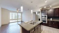 This single-floor residence is thoughtfully designed with a cohesive blend of materials and finishes throughout. The entry hallway, finished with light ceramic tile, leads into the open-concept kitchen and living area. The kitchen serves as a central feature, showcasing rich dark-wood cabinetry with sleek hardware, granite countertops, a tile backsplash, and a large central island equipped with a double basin sink and pendant lighting overhead. Stainless steel appliances, including a double oven and refrigerator, complete the space. Track and recessed lighting provide additional illumination.

The living area extends from the kitchen, featuring dark hardwood flooring, a ceiling fan, and large windows that allow abundant natural light and views of the surrounding area. Bedrooms are carpeted for comfort, each equipped with ceiling fans and windows fitted with blinds. One bedroom benefits from an adjoining walk-in closet with built-in shelving and hanging rods. A bathroom with tile flooring connects directly to the walk-in closet, offering a practical layout. An in-unit laundry area with a top-load washer and overhead shelving adds everyday convenience to this well-organized residence.