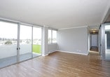 This single-floor residence offers a thoughtfully designed layout with a clean, modern aesthetic throughout. The kitchen is a standout feature, showcasing white shaker-style cabinetry, grey quartz countertops, a subway tile backsplash in soft blue-grey tones, and a full suite of stainless steel appliances including a French door refrigerator, gas range, microwave, and dishwasher. A generous island provides additional counter space and a natural gathering point. Hardwood flooring runs through the kitchen and living areas, adding warmth to the bright, neutral palette.

The living room benefits from large sliding glass doors that open to an outdoor area with tree-lined views, while a separate glass-partitioned den or flex room provides a versatile space filled with natural light. The bedrooms are carpeted for comfort and feature mirrored sliding closet doors and windows with pleasant neighborhood and treetop views.

The bathrooms are finished with white cabinetry, grey quartz countertops, and hardwood-style flooring. One bathroom includes a window with expansive views of the surrounding neighborhood and distant landscape, while another features a full tub-shower combination. Crown molding and baseboard heating are consistent details found throughout the space.