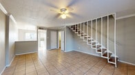 This two-story home offers a well-organized layout spread across two floors, providing a comfortable and functional living environment. The main level features an open living area finished with large-format tile flooring and a ceiling fan with light fixture, creating a bright and airy atmosphere. An open staircase with wood treads and white balusters serves as a central architectural element, connecting the two floors with a clean, contemporary look. The kitchen is galley-style, equipped with white cabinetry, gray laminate countertops, a double-basin sink, and stainless steel appliances including a refrigerator and range. A window provides natural light to the space.

The upper floor hosts both bedrooms, each featuring wood-look laminate flooring and ceiling fans. The primary bedroom offers a generous footprint with its own closet and a private en-suite bathroom. The en-suite bath includes a single-sink vanity with gray countertops, white cabinetry, and a tiled shower surround. The second bedroom is equally well-appointed with its own closet and access to a full hallway bathroom, which mirrors the same vanity style. Both floors include hallways and closets that contribute to practical storage and circulation throughout the home.