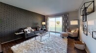This single-floor, two-bedroom, two-bathroom residence at Verona combines modern finishes with distinctive architectural character throughout. The living area serves as the heart of the home, anchored by a striking dark exposed brick accent wall that adds texture and visual depth. Hardwood-style flooring runs throughout the space, complementing the neutral color palette. A sliding glass door floods the living room with natural light while providing direct access to an outdoor patio with views of surrounding greenery.

The kitchen is thoughtfully designed with dark espresso cabinetry, quartz countertops, a mosaic tile backsplash, and stainless steel appliances including a range, microwave, and dishwasher. An open-rail partition connects the kitchen to the living area, creating a cohesive flow between spaces.

Both bedrooms are generously sized, each featuring large windows that invite natural light and sliding closet doors for ample storage. The primary bedroom includes an en-suite bathroom with a dark-framed vanity mirror, espresso cabinetry, and stone-topped counters. The second bathroom offers a full tub-shower combination and matching hardwood-style flooring, maintaining a consistent, polished aesthetic throughout the residence.