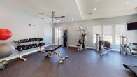 Located at 22 Evesboro-Medford Road in Medford, NJ, this single-floor fitness center is thoughtfully designed to support a comprehensive workout experience. The space is organized into distinct functional zones, all unified by a clean, modern aesthetic featuring soft gray walls, white trim, and durable rubber flooring throughout.

The cardio area is well-appointed with multiple treadmills, a stationary bike, and a rowing machine, all positioned in front of large windows fitted with roller shades that allow ample natural light while maintaining comfort. Wall-mounted flat-screen televisions are strategically placed to keep users engaged during cardio sessions.

The strength training zone features a full Hoist cable machine system, a multi-functional weight bench, and a tiered dumbbell rack with a wide range of free weights. Additional Hoist selectorized machines provide users with targeted resistance training options.

A separate studio or functional training area is accessible through glass-paneled doors and is stocked with stability balls, resistance bands, medicine balls, and other accessories for flexibility and functional fitness. Ceiling fans in select areas enhance air circulation, while recessed lighting ensures the entire space is well-lit. The layout offers an open, spacious feel that accommodates multiple users simultaneously with ease.
