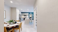 This single-story residence offers a thoughtfully arranged floor plan with two bedrooms, two bathrooms, and two closets across a comfortable footprint. The open-concept living area seamlessly connects the kitchen, dining, and living spaces, creating a cohesive and functional hub for daily life. The kitchen is a standout feature, equipped with stainless steel appliances, a built-in microwave, and an abundance of light gray shaker-style cabinetry. A central island with a white countertop provides both additional workspace and casual seating. Light wood-look flooring runs throughout, complementing the neutral wall tones and recessed lighting overhead. A bold teal accent wall bridges the kitchen and living room, adding a vibrant focal point to the space. The dining area is defined and intimate, with room for a round table and seating. The primary bedroom is generously sized, offering natural light from large windows, a ceiling fan, and a walk-in closet with wire shelving. Both bathrooms are finished with white countertops, one featuring distinctive blue cabinetry and globe lighting. The second bedroom also benefits from natural light and ample window space, maintaining the home's bright and contemporary character throughout.