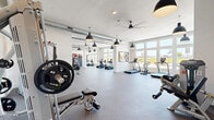 Located at 17501 Dallas Parkway in Dallas, Texas, this fitness center offers a generously sized, single-floor layout designed to accommodate a wide range of workout styles and fitness goals. The space features crisp white walls, durable speckled rubber flooring, and high ceilings with exposed ductwork that lend an open, modern-industrial aesthetic. Multiple ceiling fans and pendant light fixtures provide both comfort and ample illumination throughout.

Large windows along the perimeter flood the interior with natural light while offering views of the surrounding landscape, creating an energizing atmosphere. The floor plan is thoughtfully organized into distinct zones. The cardio area is lined with treadmills and cycling machines, while the strength training section houses cable machines, a functional trainer, weight benches, and a comprehensive free weight rack with dumbbells spanning a wide range. A dedicated functional training zone features a Torque multi-purpose rig complete with a heavy punching bag, kettlebells, medicine balls, and stability balls.

Full-length mirrors are positioned throughout, enhancing the sense of space and supporting proper form during workouts. A water station is conveniently available on-site. The overall ambiance is clean, bright, and professional, making this fitness center a comprehensive facility well-suited for both casual users and serious athletes.