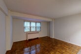 Located at 3435 Holmead Pl NW in Washington, DC, this efficiently designed unit makes thoughtful use of its compact footprint. The living room serves as the heart of the space, showcasing rich parquet hardwood flooring with a warm, polished finish that runs throughout the unit. A multi-pane window with horizontal blinds allows natural light to fill the room, while a radiator beneath the window provides in-unit heating. The open layout connects the living area to a functional kitchen, which features white cabinetry, a gas range, and a full-size refrigerator, along with light-toned flooring that contrasts with the parquet in the main area. A hallway leads from the living space toward the bathroom and two closets, offering practical storage options. The bathroom is finished with full white subway tile wainscoting, a white vanity with under-cabinet storage, a wall-mounted mirror, and textured walls above the tile line. The entry hallway provides a clear transition into the main living area. Throughout the unit, neutral white walls and clean lines contribute to a simple, functional aesthetic suited for urban living in the Columbia Heights neighborhood of Washington, DC.