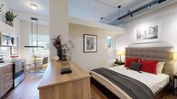 Located at 111 Martine Ave in White Plains, NY, this single-floor unit offers a thoughtfully designed open-concept layout with a distinctly modern, loft-inspired aesthetic. Soaring ceilings with exposed ductwork lend an industrial character throughout, while warm hardwood flooring grounds the space with a natural, inviting feel.

The living area is bright and welcoming, featuring large windows that frame views of the surrounding White Plains cityscape and allow generous natural light to fill the room. Bold, eclectic artwork — including a striking Andy Warhol-inspired triptych — adds a vibrant, artistic personality to the space.

The kitchen is sleek and fully functional, outfitted with stainless steel appliances including a refrigerator, range, microwave, and dishwasher. White upper cabinetry is paired with warm wood-toned lower cabinets, a marble-effect tile backsplash, and under-cabinet lighting, creating a polished yet practical cooking environment. Potted greenery displayed atop the cabinetry adds a lively, organic touch.

The sleeping area is seamlessly integrated within the open floor plan, with a wood dresser serving as a natural divider between spaces. The bathroom features clean, light-toned tile work, a wood-finish vanity, and contemporary fixtures, offering a calm, spa-like retreat. Overall, the space combines urban sophistication with warm, curated design details.