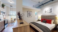 Located at 111 Martine Ave in White Plains, NY, this single-floor unit offers a thoughtfully designed open-concept layout with a distinctly modern, loft-inspired aesthetic. Soaring ceilings with exposed ductwork lend an industrial character throughout, while warm hardwood flooring grounds the space with a natural, inviting feel.

The living area is bright and welcoming, featuring large windows that frame views of the surrounding White Plains cityscape and allow generous natural light to fill the room. Bold, eclectic artwork — including a striking Andy Warhol-inspired triptych — adds a vibrant, artistic personality to the space.

The kitchen is sleek and fully functional, outfitted with stainless steel appliances including a refrigerator, range, microwave, and dishwasher. White upper cabinetry is paired with warm wood-toned lower cabinets, a marble-effect tile backsplash, and under-cabinet lighting, creating a polished yet practical cooking environment. Potted greenery displayed atop the cabinetry adds a lively, organic touch.

The sleeping area is seamlessly integrated within the open floor plan, with a wood dresser serving as a natural divider between spaces. The bathroom features clean, light-toned tile work, a wood-finish vanity, and contemporary fixtures, offering a calm, spa-like retreat. Overall, the space combines urban sophistication with warm, curated design details.