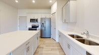 This well-appointed two-story home offers a thoughtfully designed layout spread across two levels, connected by a central staircase. The main level features a welcoming entryway with a paneled front door and large windows that flood the open living area with natural light. Views of the surrounding neighborhood and green lawn are visible from the front-facing windows. The kitchen is a standout space, showcasing light gray shaker-style cabinetry, a central island with a clean white countertop, wood-look tile flooring, and stainless steel appliances including a range, microwave, and French door refrigerator. A dedicated laundry room on the main level is equipped with a full-size washer and dryer and overhead shelving for added storage. Upstairs, the bedrooms are finished with plush wall-to-wall carpeting and feature windows with neighborhood views. One bedroom includes a spacious walk-in closet outfitted with custom built-in shelving, hanging rods, and integrated drawers — offering generous organization solutions. A full bathroom with a single-sink vanity, tub-shower combo, and tile flooring serves the upper level. Throughout, the home maintains a neutral, bright palette with white walls, recessed lighting, and ceiling fans, creating a clean and cohesive living environment.