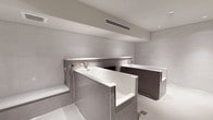 This meticulously designed bathroom space presents a refined, spa-like aesthetic defined by a cohesive neutral palette and high-quality finishes throughout. The single-level layout is anchored by two deep soaking tubs, each encased in grey subway tile surrounds that serve as a defining architectural element. Wall-mounted chrome fixtures accompany each tub, contributing to the clean, uncluttered design language.

The walls feature a combination of large-format light grey tiles and smaller mosaic stone tiles, visible through a sleek black-framed glass partition that delineates a separate wet area. This partition adds a contemporary architectural detail while maintaining a sense of openness. A built-in tiled bench provides a functional and elegant seating element within the wet zone.

The flooring is finished in a speckled light grey material that complements the surrounding tile work. Recessed ceiling lights and a linear HVAC vent are integrated cleanly into the smooth ceiling, ensuring both comfort and a streamlined appearance. The overall ambiance is calm and minimalist, evoking a high-end wellness environment with careful attention to material consistency and spatial flow.