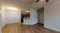 This single-floor residence offers a well-designed open-concept layout that seamlessly connects the living area and kitchen, creating a functional and inviting space. The main living area features warm hardwood-style flooring, crown molding, and a ceiling fan with a light fixture, contributing to a comfortable and polished atmosphere. An elegant chandelier in the dining area adds a refined touch.

The kitchen is a standout feature, appointed with rich dark wood cabinetry, granite-look countertops, a classic white subway tile backsplash, and a full suite of black appliances including a refrigerator, range, microwave, and dishwasher. A peninsula breakfast bar provides additional prep space and casual dining. Track lighting illuminates the kitchen efficiently.

The bedroom is generously sized, finished with plush carpet flooring, a ceiling fan, and a glass door that opens to an outdoor area, allowing natural light to fill the room. A hallway leads to a bathroom, visible from the bedroom corridor.

Throughout the space, neutral gray walls provide a versatile backdrop, while white baseboards and trim offer clean contrast. The single-floor layout ensures ease of navigation, making this a practical and comfortable living space overall.