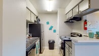 This single-floor unit is thoughtfully laid out to maximize functionality across its key living areas. The galley-style kitchen is efficiently designed with upper and lower cabinetry, dark laminate countertops, a mosaic tile backsplash, and stainless steel appliances including a refrigerator and electric range with overhead ventilation. Light tile flooring runs underfoot, and the kitchen opens toward the living area via a breakfast bar with counter seating, creating a natural connection between cooking and dining spaces.

The living area is bright and welcoming, with a window allowing natural light to fill the room. Light tile flooring continues from the kitchen, and the space comfortably accommodates a sectional sofa and area rug. A textured ceiling is consistent throughout the unit.

The bedroom features light wood-look laminate flooring, a ceiling fan with integrated lighting, and two closets offering practical storage. The neutral gray walls create a calm, restful atmosphere.

The bathroom is finished with light tile flooring and includes a tub-shower combination with tile surround, a toilet, and a vanity. Decorative wall accents add a personal touch just outside the bathroom entrance, rounding out this well-organized and functional living space.