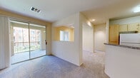 Located at 4800 Tassajara Rd in Dublin, CA, this well-appointed one-bedroom, one-bathroom residence offers a thoughtfully designed single-level layout. The combined kitchen and living room serves as the heart of the home, where a peninsula with granite-style countertops separates the kitchen from the living area. The kitchen is equipped with light wood cabinetry, a white appliance suite including a refrigerator, microwave, and range, and recessed lighting overhead. The living area features plush carpeting and a sliding glass door that opens to a private balcony with outdoor views, allowing natural light to fill the space. An arched hallway connects the main living area to the private bedroom, which is generously sized with large windows that frame greenery outside, soft carpet flooring, and ample wall space. The bedroom includes a walk-in closet with dual hanging rods and shelving for organized storage. The bathroom offers a full tub-shower combination with white tile surround and clean, neutral finishes. A dedicated in-unit laundry area accommodates a full-sized washer and dryer side by side. Throughout, warm beige tones and neutral walls create a bright, cohesive ambiance.