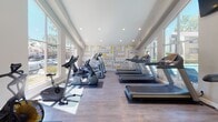 This single-story fitness center is thoughtfully designed to support a comprehensive workout experience. The space is divided into two connected zones: a main cardio area and a dedicated strength training section, linked by an open passage that maintains a sense of flow throughout.

The main cardio area is bright and airy, benefiting from soaring ceilings accented by a ceiling fan and warm yellow walls. Large windows along multiple walls flood the space with natural light and provide views of the surrounding outdoor areas, including a pool and neighboring grounds. The wood-style flooring runs throughout, lending a clean, cohesive look. A row of treadmills lines one wall, accompanied by elliptical trainers from Precor and stationary bikes, all positioned to take advantage of the outdoor views. A wall-mounted TV adds convenience for users during workouts.

A bold motivational typography mural serves as a striking accent wall in the cardio zone, featuring fitness-themed words in yellow and gray. The adjoining strength training area houses cable machines, free weights, medicine balls, and functional training equipment such as a tire, housed under recessed lighting. The overall ambiance is energetic, well-lit, and inviting.