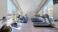 This single-story fitness center is thoughtfully designed to support a comprehensive workout experience. The space is divided into two connected zones: a main cardio area and a dedicated strength training section, linked by an open passage that maintains a sense of flow throughout.

The main cardio area is bright and airy, benefiting from soaring ceilings accented by a ceiling fan and warm yellow walls. Large windows along multiple walls flood the space with natural light and provide views of the surrounding outdoor areas, including a pool and neighboring grounds. The wood-style flooring runs throughout, lending a clean, cohesive look. A row of treadmills lines one wall, accompanied by elliptical trainers from Precor and stationary bikes, all positioned to take advantage of the outdoor views. A wall-mounted TV adds convenience for users during workouts.

A bold motivational typography mural serves as a striking accent wall in the cardio zone, featuring fitness-themed words in yellow and gray. The adjoining strength training area houses cable machines, free weights, medicine balls, and functional training equipment such as a tire, housed under recessed lighting. The overall ambiance is energetic, well-lit, and inviting.