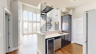 Located in the heart of Hollywood at 6138 Franklin Ave, this two-story, 2-bedroom, 2-bathroom home offers a striking blend of modern design and functional living. The main floor commands attention with soaring double-height ceilings and a wall of floor-to-ceiling windows that flood the living area with abundant natural light. A sculptural black spiral staircase serves as a dramatic architectural centerpiece, seamlessly connecting the two levels. The open kitchen features dark cabinetry, white countertops, stainless steel appliances including a refrigerator, gas range, dishwasher, and a built-in wine cooler, complemented by warm hardwood flooring carried throughout the home. Both bedrooms are well-proportioned, finished with neutral tones, hardwood floors, and ceiling fans, with natural light streaming through slatted blinds. The two bathrooms are appointed with dark vanity cabinetry, marble-style countertops, large-format tile flooring, and tub-shower combinations — one featuring a heated towel rack. Additional closet and hallway spaces provide practical storage throughout. The upper level offers a more intimate retreat, rounding out a thoughtfully designed home that balances volume, light, and livability in a prime Los Angeles location.