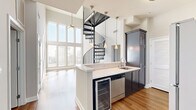 Located in the heart of Hollywood at 6138 Franklin Ave, this two-story, 2-bedroom, 2-bathroom home offers a striking blend of modern design and functional living. The main floor commands attention with soaring double-height ceilings and a wall of floor-to-ceiling windows that flood the living area with abundant natural light. A sculptural black spiral staircase serves as a dramatic architectural centerpiece, seamlessly connecting the two levels. The open kitchen features dark cabinetry, white countertops, stainless steel appliances including a refrigerator, gas range, dishwasher, and a built-in wine cooler, complemented by warm hardwood flooring carried throughout the home. Both bedrooms are well-proportioned, finished with neutral tones, hardwood floors, and ceiling fans, with natural light streaming through slatted blinds. The two bathrooms are appointed with dark vanity cabinetry, marble-style countertops, large-format tile flooring, and tub-shower combinations — one featuring a heated towel rack. Additional closet and hallway spaces provide practical storage throughout. The upper level offers a more intimate retreat, rounding out a thoughtfully designed home that balances volume, light, and livability in a prime Los Angeles location.