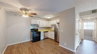 Located at 111 Whitsett Rd in Nashville, TN, this single-story, 2-bedroom, 1-bathroom home offers a practical and functional layout across a compact footprint. The open-plan kitchen and living area form the heart of the home, featuring durable wood-style flooring throughout and a ceiling fan with light fixture. The kitchen is equipped with white cabinetry, yellow laminate countertops, a black electric range with overhead ventilation, a stainless steel refrigerator, and a double-basin sink — all set against a textured ceiling. The living room provides a clean, open space with a front entry door and a sliding glass door that brings in natural light and outdoor access. The primary bedroom is a well-proportioned room with plush carpeting, a textured ceiling, and the notable feature of dual closets, offering generous storage space. The second bedroom also features carpeting and closet space. The bathroom is appointed with a combined tub and shower unit, a vanity with a light countertop, and wood-style flooring. Neutral gray wall tones are carried throughout the home, creating a cohesive and understated aesthetic that suits a variety of furnishing styles.