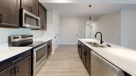 Located at 220 E Johnson Cir in Clarksville, Tennessee, this single-floor home offers a well-designed layout with a consistent modern aesthetic throughout. The kitchen is a standout feature, showcasing rich dark cabinetry, white countertops, and a full suite of stainless steel appliances including a range, microwave, refrigerator, and dishwasher. A large island with an undermount sink and stylish pendant lighting adds both functionality and visual appeal. Light wood-look flooring runs through the main living areas, complementing the neutral wall tones and bright, open feel of the space. The living area is generously sized with a ceiling fan and direct access to the front entry. The bedrooms feature plush carpeting, ceiling fans, and natural light from windows with neighborhood views. Each bedroom offers access to a closet, providing practical storage. Two full bathrooms mirror each other in design, each appointed with dark vanity cabinetry, white countertops, large mirrors, and tile-accented shower and tub surrounds, with matching light wood-look flooring. A dedicated laundry room houses a full-size washer and dryer with overhead wire shelving for additional storage. The home presents a clean, move-in-ready condition with cohesive finishes throughout.