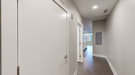 Located at 55 SW Ottawa Ave in downtown Grand Rapids, Michigan, this two-bedroom, two-bathroom unit offers a well-designed open-concept layout across a single floor. The kitchen serves as the centerpiece of the living space, showcasing white shaker cabinetry, a mosaic tile backsplash, dark countertops, stainless steel appliances including a refrigerator, range, and microwave, and a central island with a sink — all illuminated by stylish track lighting overhead. Dark hardwood-style flooring extends throughout the main living and kitchen areas, lending a sleek, contemporary feel. A hallway connects the main living area to the private quarters, where both bedrooms feature plush carpeting and neutral gray walls. The primary bedroom is a comfortable size with access to a dedicated closet, while a large window in the secondary bedroom frames views of the surrounding urban streetscape. Each of the two bathrooms is finished with white cabinetry topped with dark counters, chrome fixtures, and a full tub-shower combination. Clean lines, a neutral color palette, and modern finishes throughout create a cohesive and polished aesthetic well-suited to urban living in the heart of Grand Rapids.