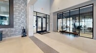 Located at 902 Town Center Blvd in Garland, Texas, this single-floor clubhouse for Soltra Firewheel is a thoughtfully designed community amenity space that blends modern architecture with warm, inviting interiors. The space makes an immediate impression with its soaring double-height ceilings, exposed wood beam detailing, and large-format light tile flooring accented by contrasting darker inlays.

The grand corridor entrance leads residents through a series of distinct zones, each defined by floor-to-ceiling glass partitions with bold black steel framing. The leasing office greets visitors with sputnik pendant lighting, vertical wood slat wall panels, and sleek workstations set against abundant natural light from expansive windows.

The main lounge area serves as the social heart of the clubhouse, featuring a linear fireplace flanked by a curated art piece, plush seating arrangements, and oversized pendant lighting. Adjacent to the lounge, a game area includes a full billiards table and a shuffleboard, offering a lively recreational retreat.

A co-working zone with high-top tables sits behind glass walls, providing a bright and focused workspace with views of the surrounding Firewheel community. Throughout, accent walls with textured stone-inspired patterns and rich wood ceilings add depth and character, creating an upscale yet welcoming atmosphere.