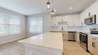 Located at 5236 Legendary Loop in Wesley Chapel, FL, this well-appointed single-story home offers three bedrooms, two bathrooms, and a thoughtfully designed layout. The open-concept living and kitchen area serves as the heart of the home, featuring light wood-tone luxury vinyl plank flooring, large windows with blinds that invite abundant natural light, and a seamless flow between spaces. The kitchen stands out with crisp white upper cabinetry, warm natural wood lower cabinets, a herringbone tile backsplash, stainless steel appliances, and a spacious island topped with a bright white quartz surface, illuminated by stylish globe pendant lights. The primary bathroom is finished with wood-tone vanity cabinetry, matte black hardware, a white quartz countertop, and a glass-enclosed walk-in shower with marble-style tile surround. The second bathroom mirrors the same design aesthetic and includes a soaking tub. All three bedrooms feature soft neutral carpet, ceiling fans, and generous windows. The primary bedroom includes a walk-in closet with multi-level wire shelving. Three total closets provide ample storage throughout. Clean lines, a neutral palette, and modern finishes create a cohesive, contemporary ambiance across the entire home.