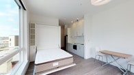 This thoughtfully designed studio unit maximizes every square foot through smart space planning and modern finishes. The open-plan layout seamlessly integrates the sleeping, dining, and kitchen areas into a cohesive living environment. A full-size Murphy bed with integrated shelving units on either side folds away when not in use, instantly transforming the sleeping area into usable living space — a standout feature that significantly enhances the unit's versatility.

The kitchenette is efficiently appointed with white upper cabinetry, grey lower cabinets, a single-basin sink, a built-in oven, and a full-size refrigerator, offering all the essentials within a compact footprint. A small dining table with a chair is positioned nearby, providing a dedicated space for meals or work.

Throughout the unit, crisp white walls and ceilings create a bright, airy atmosphere, complemented by recessed lighting and a clean flush ceiling fixture. Wide-plank wood-look flooring runs throughout, adding warmth and visual continuity to the space. The overall aesthetic is contemporary and minimalist, making this studio a practical and well-finished living option.