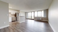 This single-floor unit offers a clean, modern aesthetic throughout its thoughtfully designed layout. The open-concept living and dining area is anchored by wide-plank light wood flooring and a textured ceiling, creating a welcoming, airy atmosphere. Floor-to-ceiling windows span the length of the main living space, flooding the interior with natural light and providing sweeping outdoor views, with access to a balcony beyond the glass.

The kitchen is seamlessly integrated into the living area via a peninsula island, offering a functional and social layout. White shaker-style cabinetry, light countertops, and a full suite of stainless steel appliances — including a refrigerator, dishwasher, microwave, and range — give the kitchen a contemporary, polished look.

The bedroom is generously proportioned, featuring plush wall-to-wall carpeting, neutral toned walls, and a dedicated wall-unit climate control system, alongside a window that brings in natural light.

Two bathrooms serve the unit: one features a crisp white vanity with modern chrome fixtures, a large mirror, and tiled flooring; the other is a clean, simply appointed space with tiled floors and a tub-shower combination. Throughout the unit, the neutral color palette and consistent finishes contribute to a cohesive, move-in-ready environment.
