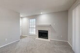 This 2-bedroom, 2-bathroom apartment at Legacy Apartments in Plano, Texas offers a well-organized single-floor layout designed for comfortable everyday living. The living room serves as the heart of the home, featuring plush carpeting, a tile-surround wood-burning fireplace with a white mantel, and large sliding glass doors fitted with vertical blinds that flood the space with natural light and provide access to an outdoor area with views of surrounding greenery. A dedicated dining room sits adjacent to the kitchen, which is equipped with dark espresso cabinetry, a mosaic tile backsplash, light stone countertops, black appliances including a refrigerator, electric range, and over-the-range microwave, and wood-look flooring. A pantry provides additional storage nearby. Both bedrooms are carpeted and receive natural light through sizable windows with blinds; the primary bedroom is generously proportioned and includes a ceiling fan with light fixture. Each of the two bathrooms features a full tub-and-shower combination with white tile surround. The unit also includes an in-unit laundry room and four closets for ample storage throughout. A connecting hallway ties the layout together efficiently, completing this functional and comfortable residence.