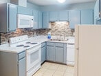 Located at 2300 Merchant Dr in Knoxville, Tennessee, this single-floor unit offers a practical and updated living space with a cohesive modern aesthetic throughout. The kitchen is a standout feature, designed in an efficient U-shaped layout with cool gray cabinetry, granite-look countertops, and a distinctive mosaic tile backsplash in warm earth tones. White appliances — including a coil-burner electric range, over-the-range microwave, dishwasher, and refrigerator — provide full functionality. Light tile flooring completes the kitchen's clean look. The living area transitions to durable wood-look plank flooring set against soft gray walls and textured ceilings, creating a warm, grounded atmosphere. A window allows natural light to fill the space. An adjacent dining area features light tile flooring and a pendant light fixture, seamlessly connecting to the living space through an open layout. The bathroom is well-appointed with a wide vanity topped with a speckled countertop, dark-framed mirror, and a multi-bulb vanity light. A separate water closet area includes a tub-shower combination and tile flooring, offering a clean and functional design throughout.