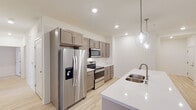 This single-floor residence showcases a thoughtfully designed open-concept layout with light hardwood flooring that flows seamlessly throughout the living spaces. The kitchen serves as a central highlight, featuring taupe shaker-style cabinetry with brushed metal hardware, crisp white quartz countertops, and a full suite of stainless steel appliances, including a French door refrigerator, electric range, and built-in microwave. A central island with an undermount double sink and elegant pendant lighting above adds both functionality and visual appeal, while recessed lighting ensures the space remains bright and welcoming.

The bedrooms are generously proportioned, each offering large windows fitted with blinds that invite abundant natural light and outdoor views of surrounding greenery. The neutral, cream-toned walls provide a clean, versatile backdrop throughout.

Two well-appointed bathrooms feature warm wood-tone vanities with white countertops, large mirrors, and striking marble-patterned tile work on floors and walls. One bathroom includes a soaking tub with a tiled surround, while the other offers a walk-in shower, both exuding a refined, spa-like aesthetic. The overall design is modern, cohesive, and move-in ready.