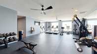 Located at 1216 N Atlantic Ave in Daytona Beach, Florida, this well-appointed fitness center offers a comprehensive workout environment designed for both cardio and strength training. The space is finished with cool light-blue walls, dark rubberized flooring, and bright white ceilings accented by sleek, modern ceiling fans that keep the atmosphere comfortable during workouts.

The main exercise area is generously proportioned and thoughtfully organized. A row of treadmills and cardio machines lines the windowed wall, bathing the space in natural light and offering views of the surrounding area. Nearby, a selection of Hoist cable and strength machines provides a full range of resistance training options. Large wall-mounted mirrors amplify the sense of space and allow for proper form checks during exercise.

A dedicated free weights section features a full dumbbell rack alongside adjustable benches, while medicine balls and additional accessories are neatly stored for functional training. A wall-mounted flat-screen television and a built-in water fountain add convenience for users. A secondary multi-purpose area with wood-tone flooring connects through the space, offering room for stretching or group activities. The hallway provides seamless access throughout the facility, completing a polished and fully equipped fitness destination.