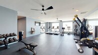Located at 1216 N Atlantic Ave in Daytona Beach, Florida, this well-appointed fitness center offers a comprehensive workout environment designed for both cardio and strength training. The space is finished with cool light-blue walls, dark rubberized flooring, and bright white ceilings accented by sleek, modern ceiling fans that keep the atmosphere comfortable during workouts.

The main exercise area is generously proportioned and thoughtfully organized. A row of treadmills and cardio machines lines the windowed wall, bathing the space in natural light and offering views of the surrounding area. Nearby, a selection of Hoist cable and strength machines provides a full range of resistance training options. Large wall-mounted mirrors amplify the sense of space and allow for proper form checks during exercise.

A dedicated free weights section features a full dumbbell rack alongside adjustable benches, while medicine balls and additional accessories are neatly stored for functional training. A wall-mounted flat-screen television and a built-in water fountain add convenience for users. A secondary multi-purpose area with wood-tone flooring connects through the space, offering room for stretching or group activities. The hallway provides seamless access throughout the facility, completing a polished and fully equipped fitness destination.