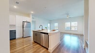 This well-appointed single-story home offers 3 bedrooms, 2 bathrooms, and a thoughtfully designed layout that maximizes both comfort and functionality. The open-concept kitchen and living area serves as the heart of the home, featuring a central island with a built-in sink and dishwasher, striking two-tone cabinetry with slate-blue lower cabinets and crisp white uppers, a subway tile backsplash, and a full suite of stainless steel appliances including a refrigerator, range, and microwave. Warm hardwood-style flooring extends throughout the main living areas, complemented by abundant natural light streaming through large windows fitted with blinds. A ceiling fan overhead adds to the comfort of the spacious living room. Each of the three bedrooms is finished with plush carpeting, a ceiling fan, and generously sized windows that bring in natural light. The primary bedroom offers a comfortable footprint with ample space. Three closets provide excellent storage throughout the home. The bathrooms are finished with wood-look tile flooring, blue-toned vanities with white countertops, and matte black hardware accents. A dedicated laundry room houses a full-size front-loading washer and dryer with built-in shelving above. The home presents a clean, modern aesthetic with a neutral palette throughout.