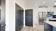 Located in Penfield, NY, this well-designed two-story home offers 2 bedrooms and 2 bathrooms across two evenly divided floors. The main level features a striking kitchen with crisp white shaker cabinetry, a bold navy blue island topped with white countertops, stainless steel appliances, and a dark subway tile backsplash. Three gold pendant lights hang above the island, adding a refined touch. Light wood-look flooring and bold black panel doors with contrasting white trim give the entryway a modern, curated aesthetic. The open living room on the upper level is a standout space, featuring a dual-ring gold chandelier, a warm wood accent wall, and sliding glass doors that open to an outdoor balcony with views of the surrounding landscape. A slate-blue accent wall and abundant natural light from multiple windows enhance the airy feel. The primary bathroom is elegantly appointed with floor-to-ceiling marble-style tile, a warm wood vanity with brass hardware, and a glass-enclosed walk-in shower. The secondary bathroom features a clean, all-white tub and shower surround. Both bedrooms are bright and comfortable, each with light flooring, neutral walls, and closet storage. Light wood-look floors run throughout the home, tying the design together cohesively.