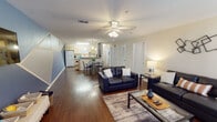 Located at 475 Appleyard Dr in Tallahassee, FL, this single-floor unit offers a functional and comfortable layout designed for everyday living. A welcoming hallway with rich, dark hardwood-style flooring leads into a spacious open-concept main living area. The living room is well-lit by a large window dressed with patterned curtains, and features a ceiling fan with integrated lighting, dark leather sofas, a glass coffee table, and contemporary wall art — creating a relaxed yet stylish atmosphere. The living space flows seamlessly into the dining area and kitchen, making it ideal for entertaining. The kitchen is outfitted with light wood cabinetry, ample counter space, and full-size white appliances including a refrigerator, electric range, and microwave. A dedicated dining area with a table and chairs sits adjacent to the kitchen. The bedroom is carpeted and features a soft blue accent wall, a ceiling fan, a full-size bed, a desk and chair for a study area, and a window with natural light. The bathroom includes a single-sink vanity with wood-toned cabinetry, a toilet, and a shower-tub combination. An in-unit washer and dryer are also present, adding to the overall convenience of this practical and inviting space.