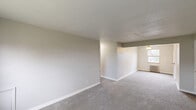Located at 1000 Vermont Ave in Castle Shannon, PA, this single-floor residence offers seven bedrooms and one bathroom within a practical, well-organized layout. The interior features neutral-toned walls and wall-to-wall carpeting throughout the living and bedroom areas, creating a consistent and easy-to-maintain aesthetic.

The spacious open living area is defined by light gray carpet, textured ceilings, and clean white baseboards. It flows into a secondary room with a ceiling fan fixture and a radiator beneath a window, allowing for natural light and classic heating. Several bedrooms are generously sized, including a notably large primary bedroom, and multiple rooms feature built-in closets with white paneled doors, offering practical storage solutions.

A central hallway connects the bedrooms and provides access to the full bathroom, which includes a tiled tub-shower combination and a frosted privacy window for natural light. The kitchen is equipped with white cabinetry, laminate countertops, a gas range, a single-basin sink, and a window overlooking the outdoors. The wood-look flooring in the kitchen provides a subtle contrast to the carpeted rooms.

Throughout the home, radiator heating units are present in several rooms, indicative of classic construction. The layout is efficient and straightforward, making this a functional multi-bedroom property in Castle Shannon.