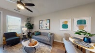 Located at 7035 Broad Way in Davenport, Polk County, Florida, this well-appointed single-floor residence offers a thoughtfully designed open-concept layout with a bright, contemporary aesthetic throughout. Light-toned luxury vinyl plank flooring flows seamlessly from the living and dining areas into the kitchen, creating a cohesive and airy feel.

The living room is a welcoming space anchored by a tufted gray sofa and accented with colorful artwork. A ceiling fan overhead and large windows fitted with blinds allow for excellent natural light and comfortable airflow. A door leads directly to a private outdoor balcony, further enhancing the sense of openness.

The kitchen is a functional and stylish highlight, featuring crisp white cabinetry with ample storage, a tile backsplash, and a full suite of stainless steel appliances including a French door refrigerator, electric range, over-the-range microwave, and dishwasher.

The bedrooms are carpeted for comfort, each offering generous natural light through large windows with blinds and ceiling fans for climate control. The neutral, warm tones of the walls create a restful atmosphere in each room.

The bathroom is cleanly finished with tile flooring, a tiled tub-shower combination, and a vanity with integrated countertop sink, providing a practical and polished space.