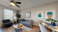 Located at 7035 Broad Way in Davenport, Polk County, Florida, this well-appointed single-floor residence offers a thoughtfully designed open-concept layout with a bright, contemporary aesthetic throughout. Light-toned luxury vinyl plank flooring flows seamlessly from the living and dining areas into the kitchen, creating a cohesive and airy feel.

The living room is a welcoming space anchored by a tufted gray sofa and accented with colorful artwork. A ceiling fan overhead and large windows fitted with blinds allow for excellent natural light and comfortable airflow. A door leads directly to a private outdoor balcony, further enhancing the sense of openness.

The kitchen is a functional and stylish highlight, featuring crisp white cabinetry with ample storage, a tile backsplash, and a full suite of stainless steel appliances including a French door refrigerator, electric range, over-the-range microwave, and dishwasher.

The bedrooms are carpeted for comfort, each offering generous natural light through large windows with blinds and ceiling fans for climate control. The neutral, warm tones of the walls create a restful atmosphere in each room.

The bathroom is cleanly finished with tile flooring, a tiled tub-shower combination, and a vanity with integrated countertop sink, providing a practical and polished space.