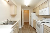 This single-floor residence offers a thoughtfully designed layout with a comfortable blend of functional spaces and practical features throughout. The open living area is generously sized, finished with plush wall-to-wall carpeting and a built-in wall shelf, and flows seamlessly into the kitchen via a breakfast bar pass-through. A ceiling fan with a light kit adds comfort to the adjoining dining or flex space.

The galley-style kitchen is well-equipped with light wood cabinetry, white appliances including a range, microwave, refrigerator, and dishwasher, and durable wood-look vinyl flooring that contrasts neatly with the neutral countertops and walls.

The bedrooms feature soft carpeting and ceiling fans, with one room showcasing a charming bay window that allows abundant natural light and outdoor views. A spacious walk-in closet with wire shelving on three walls provides ample storage.

Two bathrooms serve the residence — one featuring a single vanity with lighted mirror and tile-look flooring, and the other with a tub and shower combination enclosed by sliding frosted glass doors. A dedicated in-unit laundry room accommodates a full-size washer and dryer side by side. Throughout, neutral tones and textured ceilings create a clean, move-in-ready atmosphere.