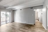 This single-floor unit offers a well-designed layout that balances open living areas with defined private spaces. The main living area is characterized by distinctive exposed beam detailing on a textured ceiling, warm wood-look flooring, and neutral-toned walls that create a clean, versatile aesthetic. A sliding glass door opens to a private balcony, allowing natural light to fill the space and providing outdoor views of surrounding greenery.

The galley-style kitchen is efficiently arranged with ample cabinetry finished in a deep slate-blue tone, light-colored countertops, a stainless steel double sink, and black appliances including a range and refrigerator. Wood-look flooring continues throughout the kitchen, maintaining a cohesive feel.

A central hallway connects the living areas to the private rooms, where the flooring transitions to plush carpet. The bedrooms feature the same beamed ceiling design, neutral walls, and windows with vertical blinds that admit generous natural light. One bedroom benefits from a larger window with outdoor views.

The bathroom presents matching dark cabinetry with a light countertop and integrated sink, consistent with the kitchen's design language. Throughout the unit, clean white baseboards, updated fixtures, and a neutral color palette contribute to a fresh, move-in-ready atmosphere.