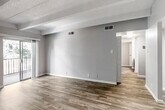 This single-floor unit offers a well-designed layout that balances open living areas with defined private spaces. The main living area is characterized by distinctive exposed beam detailing on a textured ceiling, warm wood-look flooring, and neutral-toned walls that create a clean, versatile aesthetic. A sliding glass door opens to a private balcony, allowing natural light to fill the space and providing outdoor views of surrounding greenery.

The galley-style kitchen is efficiently arranged with ample cabinetry finished in a deep slate-blue tone, light-colored countertops, a stainless steel double sink, and black appliances including a range and refrigerator. Wood-look flooring continues throughout the kitchen, maintaining a cohesive feel.

A central hallway connects the living areas to the private rooms, where the flooring transitions to plush carpet. The bedrooms feature the same beamed ceiling design, neutral walls, and windows with vertical blinds that admit generous natural light. One bedroom benefits from a larger window with outdoor views.

The bathroom presents matching dark cabinetry with a light countertop and integrated sink, consistent with the kitchen's design language. Throughout the unit, clean white baseboards, updated fixtures, and a neutral color palette contribute to a fresh, move-in-ready atmosphere.