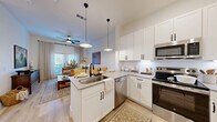 Located at 3200 Medical Center Drive in McKinney, TX, this thoughtfully designed one-bedroom, one-bathroom residence offers a cohesive open-concept layout across a single floor. Light wood flooring flows throughout, complementing the bright white walls and creating a warm, welcoming ambiance.

The kitchen is a standout feature, outfitted with white shaker cabinetry, a white subway tile backsplash, stainless steel appliances including a refrigerator with ice maker, electric range, microwave, and dishwasher, as well as a central island with a double-basin sink and seating for two. Stylish pendant lighting illuminates the island, which opens seamlessly into the living area. The living room benefits from large windows dressed with sheer linen curtains and wood blinds, allowing generous natural light while offering outdoor views.

The bedroom is a tranquil retreat featuring corner windows, sheer window treatments, and a comfortable, well-proportioned layout. An adjacent bathroom offers a soaking tub with shower, a white vanity with neutral countertops, and black hardware accents that tie back to the kitchen's design language. A dedicated closet with built-in shelving provides practical storage. A ceiling fan with light fixture serves both the kitchen/living area and the bedroom, enhancing comfort throughout.