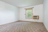 Located at 957 James St in Galena, IL, this single-floor, 2-bedroom, 1-bathroom home offers a practical and efficient layout. The kitchen features light wood cabinetry, a stainless steel sink, tile flooring, and a full-size refrigerator alongside a freestanding range, with a pass-through counter connecting it to the living area. A pendant light fixture accents the pass-through, adding a touch of warmth to the open feel between the kitchen and main living space. The carpeted living area flows naturally from the kitchen pass-through, creating a cohesive common space. Both bedrooms are carpeted and well-lit; the primary bedroom includes a wall-mounted AC unit, a window with views of surrounding greenery, and generous closet space with double bi-fold doors. The second bedroom also features a closet with built-in shelving. The bathroom is clean and functional, finished with tile flooring, a white vanity with mirrored cabinet, a toilet, and a full bathtub. Warm wood-trimmed doorframes are consistent throughout the home, lending a cohesive design element. White walls and windows in the bedrooms allow natural light to brighten the interior, contributing to an open and airy ambiance throughout this efficiently laid-out home.