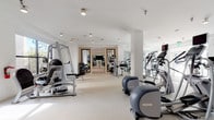 Located at 5400 S Park Terrace Ave in Greenwood Village, Colorado, this contemporary fitness center offers a thoughtfully designed, single-floor workout facility that caters to a full range of exercise needs. The space is characterized by a bright, open layout with crisp white walls, white structural columns, and light-toned flooring that together create a clean, modern aesthetic throughout.

The main gym floor is generously proportioned, accommodating an impressive array of cardio equipment including treadmills, elliptical trainers, and recumbent machines, all positioned to allow comfortable spacing between users. A dedicated strength training zone features cable machines, weight benches, and resistance equipment, providing comprehensive options for resistance-based workouts. Large mirrors along key walls enhance the sense of depth and allow exercisers to monitor their form.

A separate studio room, accessible through sleek double doors, is visible from the main floor and appears equipped for group fitness or functional training, adding further versatility to the facility. Natural light filters in through large windows, contributing to an energizing atmosphere. Motivational wall art, including bold typographic pieces and striking photographic prints, adds personality and character to the space. Recessed and track lighting ensures the entire facility remains well-illuminated throughout. The overall ambiance is polished, professional, and purpose-built for an elevated fitness experience.