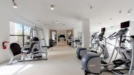 Located at 5400 S Park Terrace Ave in Greenwood Village, Colorado, this contemporary fitness center offers a thoughtfully designed, single-floor workout facility that caters to a full range of exercise needs. The space is characterized by a bright, open layout with crisp white walls, white structural columns, and light-toned flooring that together create a clean, modern aesthetic throughout.

The main gym floor is generously proportioned, accommodating an impressive array of cardio equipment including treadmills, elliptical trainers, and recumbent machines, all positioned to allow comfortable spacing between users. A dedicated strength training zone features cable machines, weight benches, and resistance equipment, providing comprehensive options for resistance-based workouts. Large mirrors along key walls enhance the sense of depth and allow exercisers to monitor their form.

A separate studio room, accessible through sleek double doors, is visible from the main floor and appears equipped for group fitness or functional training, adding further versatility to the facility. Natural light filters in through large windows, contributing to an energizing atmosphere. Motivational wall art, including bold typographic pieces and striking photographic prints, adds personality and character to the space. Recessed and track lighting ensures the entire facility remains well-illuminated throughout. The overall ambiance is polished, professional, and purpose-built for an elevated fitness experience.