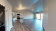 This single-floor unit showcases a thoughtfully designed open-concept layout that seamlessly connects the kitchen, dining, and living areas beneath striking vaulted ceilings. The kitchen is well-appointed with white shaker-style cabinetry, granite countertops, stainless steel appliances including a range, microwave, and refrigerator, and a central island with pendant lighting above. Wood-look luxury vinyl plank flooring runs consistently throughout the entire unit, lending a cohesive and modern aesthetic.

The living area benefits from an abundance of natural light through large sliding glass doors that open to a private balcony with outdoor views. A corner fireplace serves as a focal point in the living space, complementing the soaring vaulted ceiling. A wall-mounted mini-split unit provides additional climate control alongside baseboard heating found throughout.

The bedrooms offer comfortable proportions, with one room featuring a ceiling fan and curved wall detail. The bathroom includes a white vanity with granite countertops, a large mirror, and a separate walk-in shower with a toilet compartment. The clean, neutral color palette and modern finishes throughout create a bright, move-in-ready atmosphere.